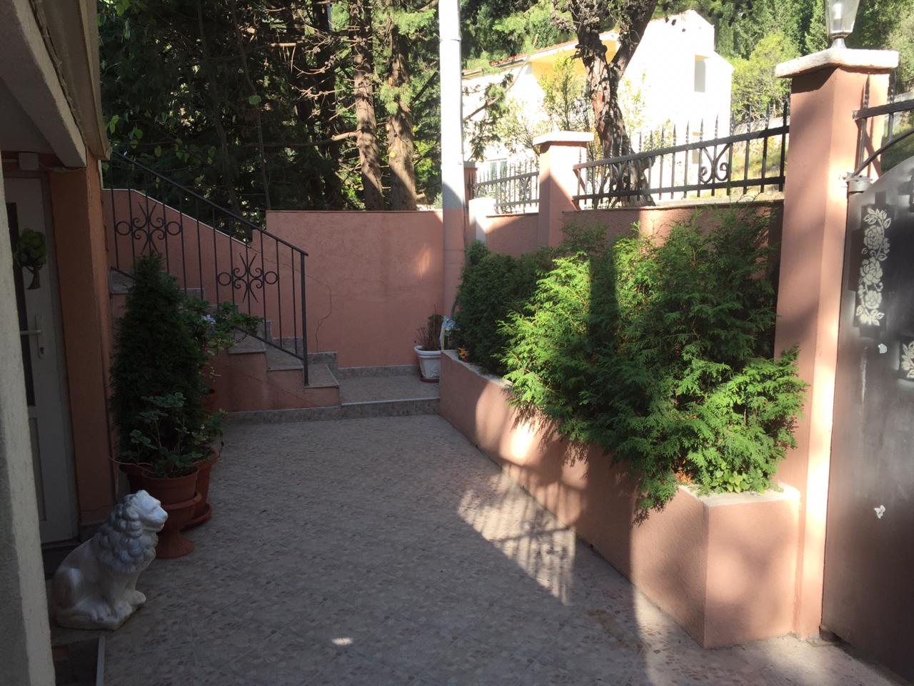 Gemütlicher Innenhof des Hauses in Šušanj, Montenegro: gepflasterte Fläche, dekorative Thuja, schmiedeeiserne Geländer und eine Löwenstatue.