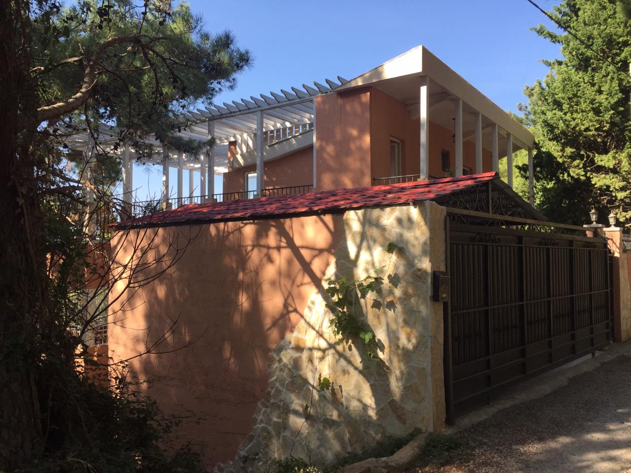 Zweistöckiges Haus in Shushan, Montenegro: Fassade mit Terrasse, Pergola und Steinverkleidung des Zauns am Einfahrtstor.