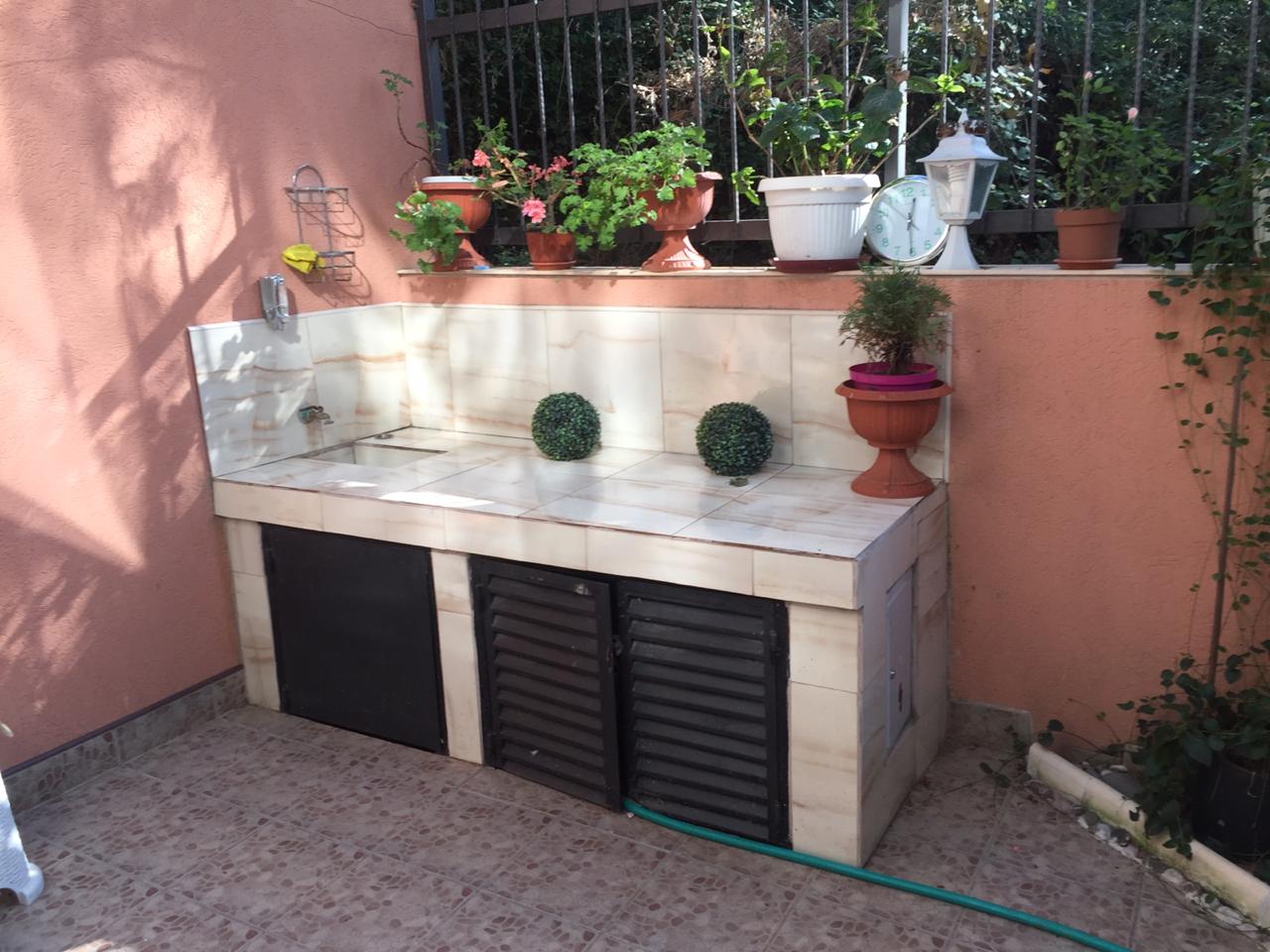 Sommerküche auf der Terrasse eines Hauses in Šušanj, Montenegro: Fliesenverkleidung, Spüle und Dekor im Garten mit lebenden Pflanzen.