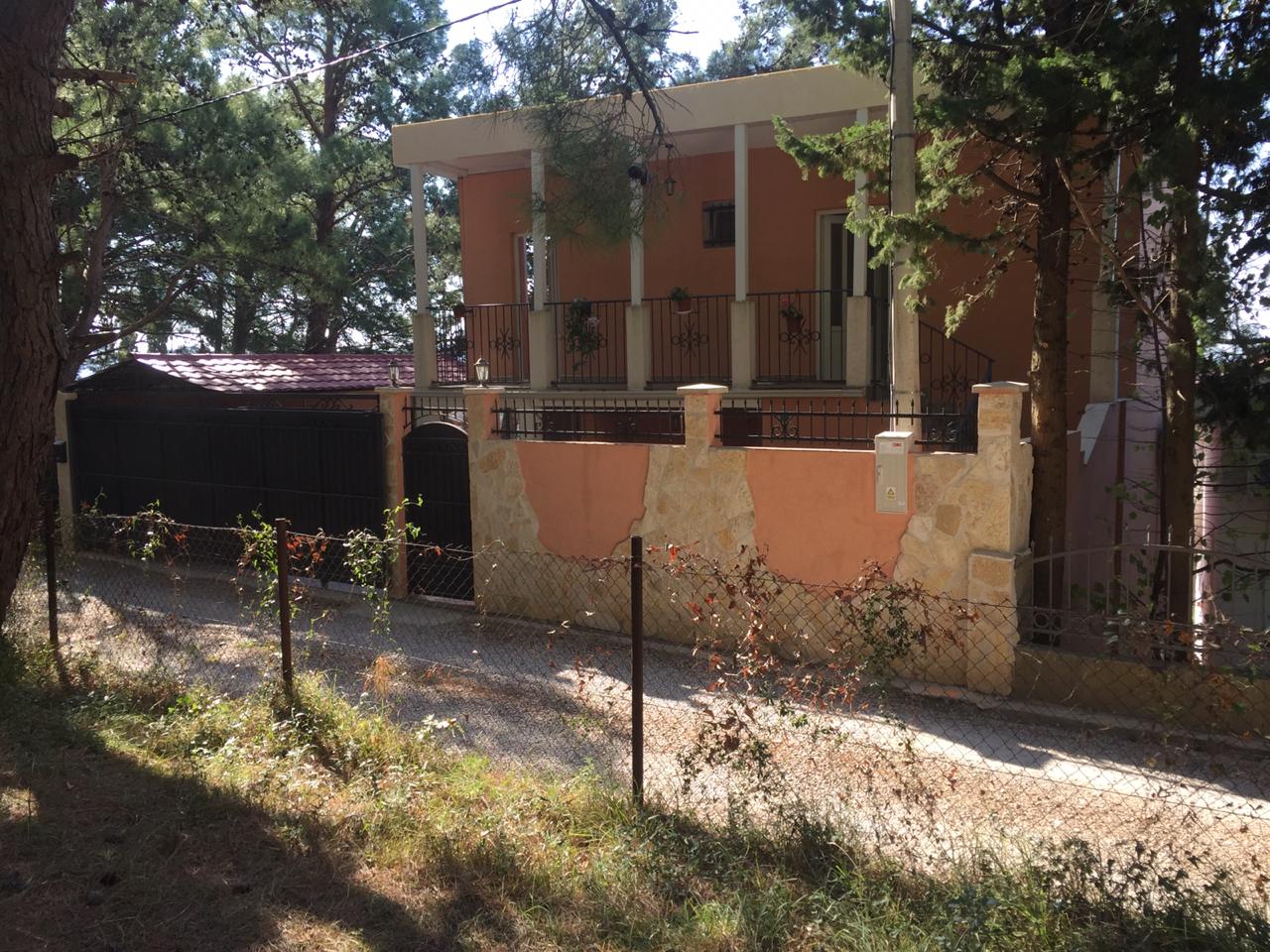 Zweistöckiges Haus mit Terrasse und Steinzaun inmitten von Kiefern, Šušanj, Montenegro. Ansicht der Fassade eines Einfamilienhauses.