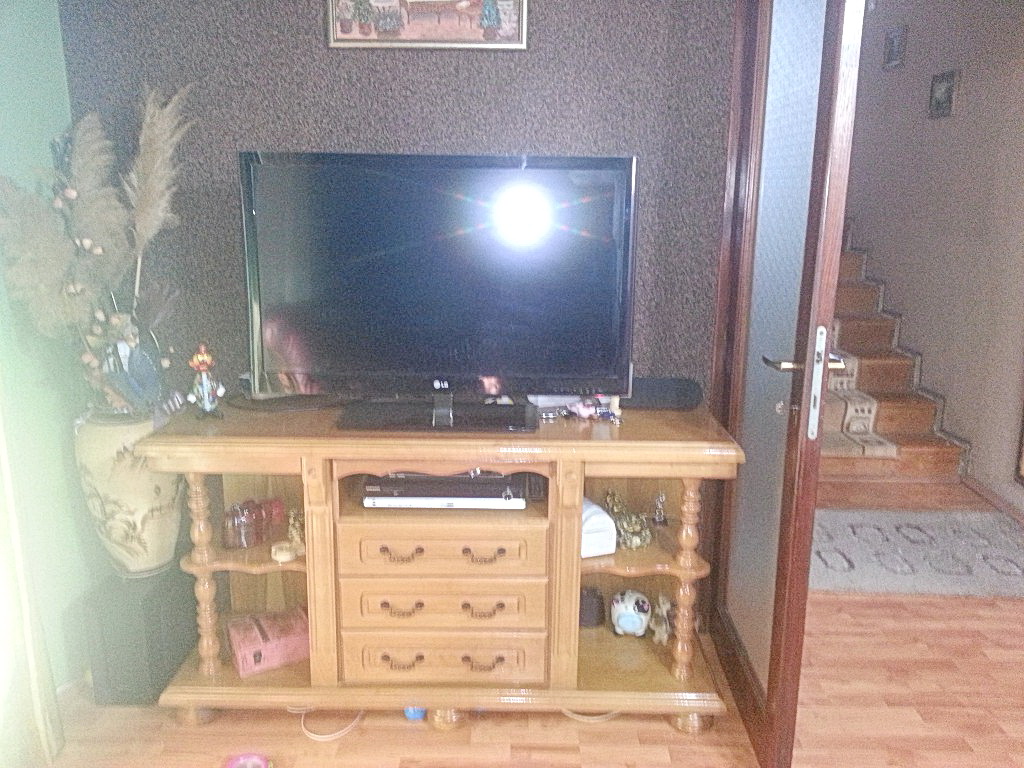 Dnevna soba u kući u Herceg Novom, Crna Gora: drvena TV komoda, dekor u vazi i pogled na stepenište u hodniku.