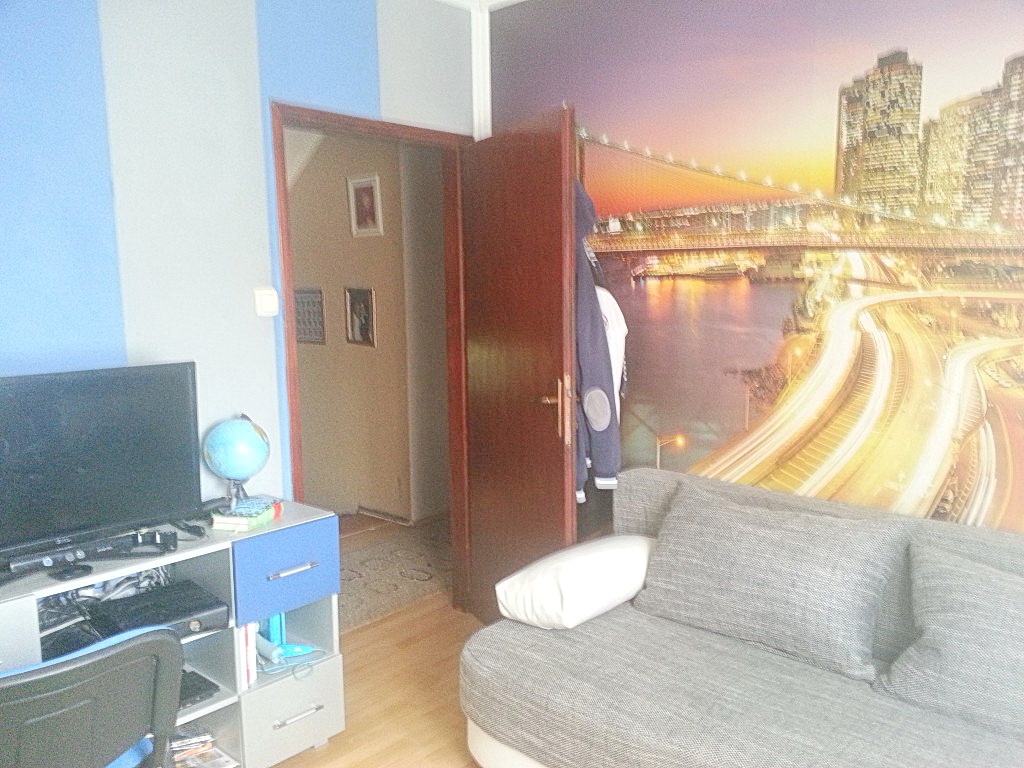 Dnevna soba u kući u Herceg Novom, Crna Gora: siva sofa, foto-tapet sa noćnim gradom i TV zona sa radnim stolom.