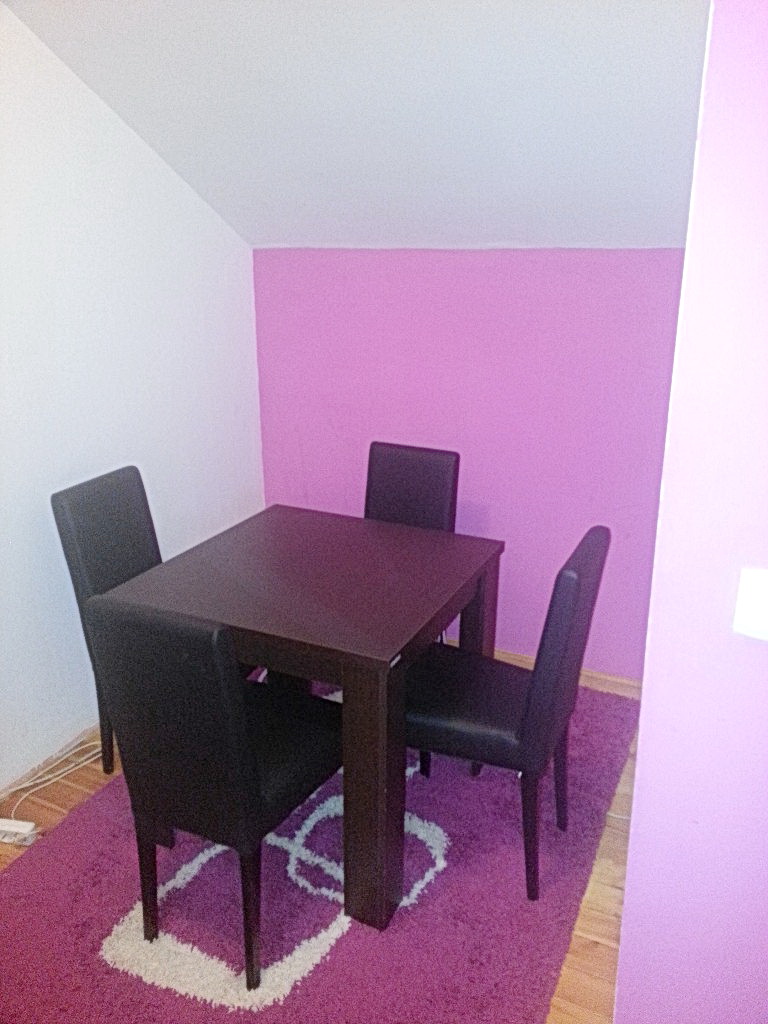 Trpezarijski deo u dnevnoj sobi kuće u Herceg Novom, Crna Gora: tamni sto, četiri stolice i ljubičasti tepih na podu.