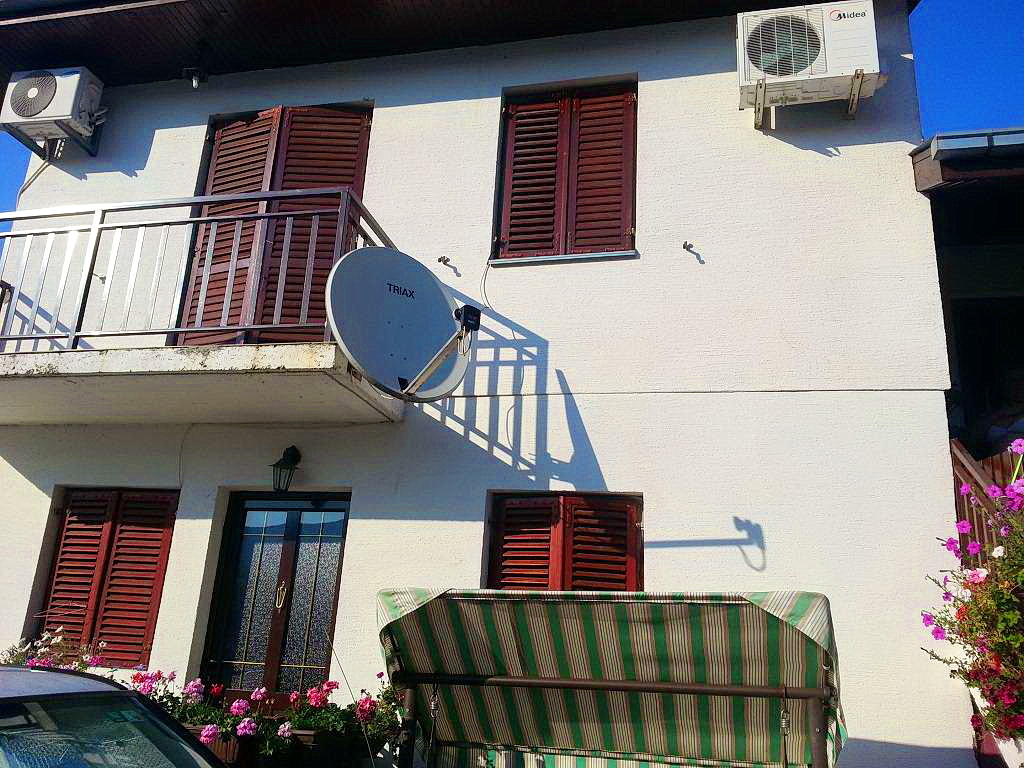 Fasada dvospratne kuće u Herceg Novom, Crna Gora: balkon, braon kapci, klima uređaji i baštenska ljuljaška.