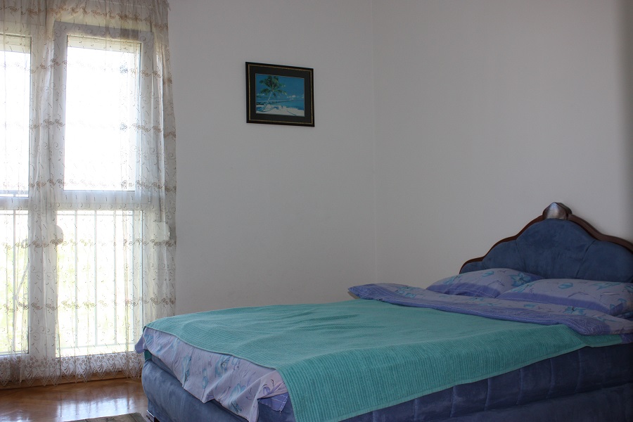 Helles Schlafzimmer mit blauem Bett und Panoramafenster in einer zum Verkauf stehenden Wohnung in Budva, Montenegro.