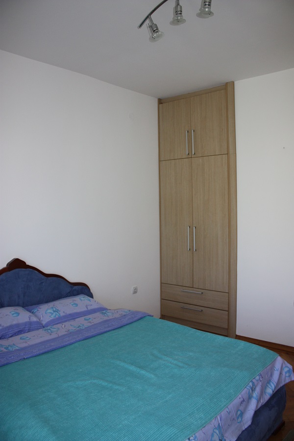 Schlafzimmer in einer Wohnung in Budva, Montenegro: Doppelbett mit blauer Tagesdecke und Einbauschrank in Holzoptik.