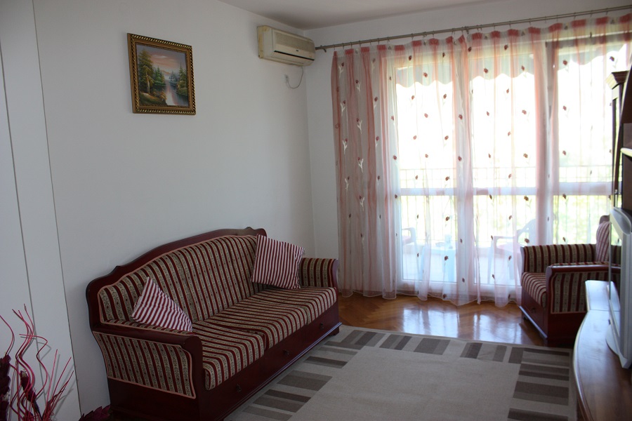 Wohnzimmer in einer Wohnung in Budva, Montenegro: gestreiftes Sofa, Parkettboden, Zugang zum Balkon und Klimaanlage.