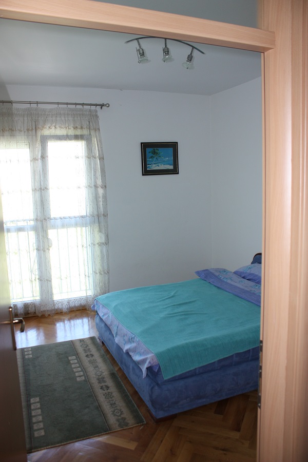 Gemütliches Schlafzimmer mit Doppelbett und Parkett in einer Wohnung in Budva, Montenegro, mit Zugang zu einem hellen Balkon.