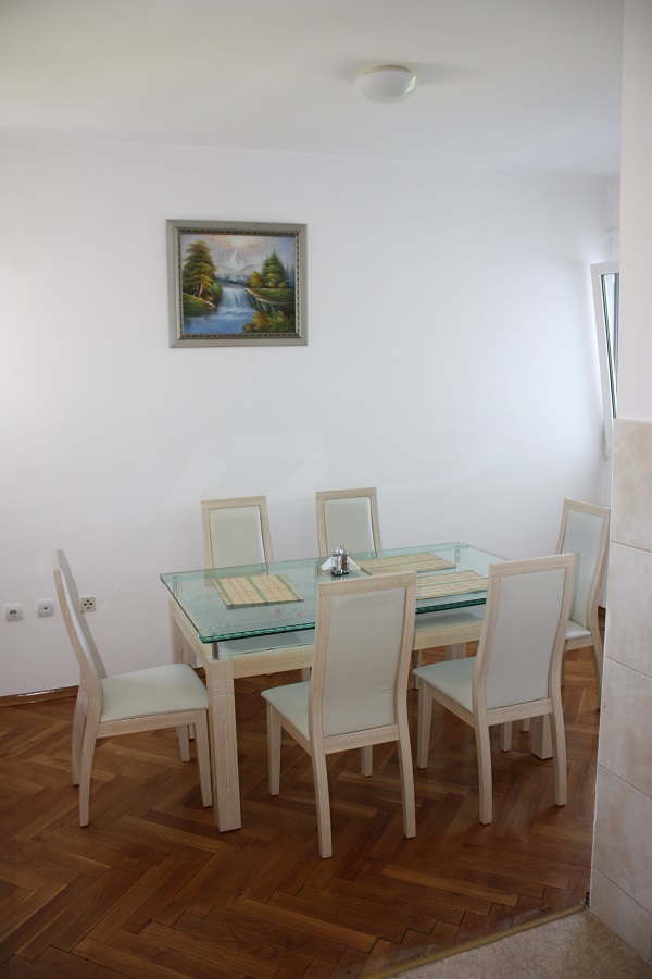 Essbereich in einer Wohnung in Budva, Montenegro: Glastisch, helle Stühle und Parkettboden im Wohnzimmer.