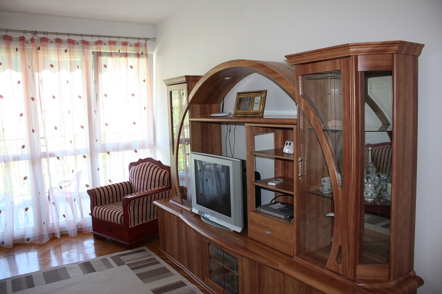 Wohnzimmer in einer Wohnung in Budva, Montenegro: Holzschrankwand, Fernseher und gestreifter Sessel am Panoramafenster.