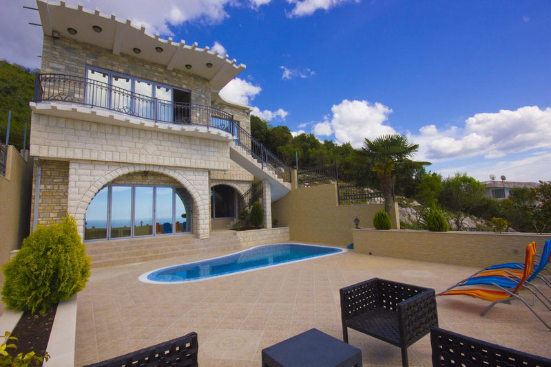 Karadağ, Dobra Voda’da havuzlu ve teraslı iki katlı villa: taş kaplama, panoramik pencereler ve deniz manzarası.