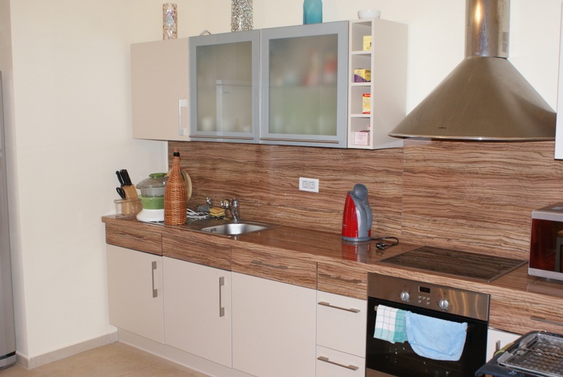 Moderne Küche in einem Haus in Bigovo, Montenegro: helle Einbauküche, Holzoptik-Arbeitsplatte, integrierte Geräte und Dunstabzugshaube.