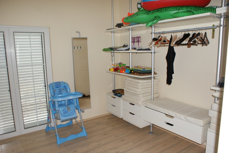 Ankleidezimmer mit offenen Regalen und einem Kinderstuhl in einem Haus in Bigovo, Montenegro. Helles Interieur mit Laminatboden.