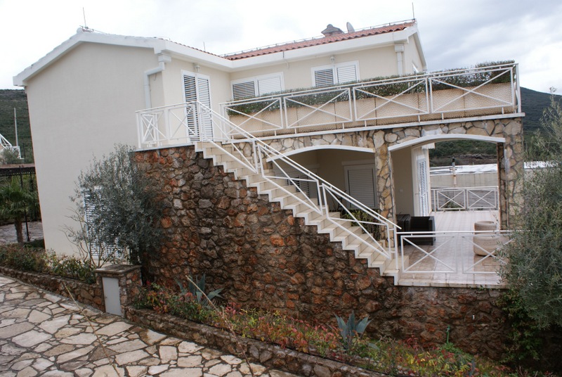 Zweistöckiges Haus in Bigovo, Montenegro: Fassadenverkleidung aus Stein, Außentreppe, Terrasse und Balkon mit weißen Geländern.
