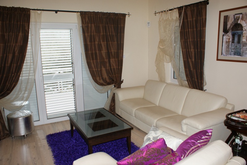 Gemütliches Wohnzimmer in einem Haus in Bigovo, Montenegro: helles Ledersofa, Glastisch und Panoramatür.