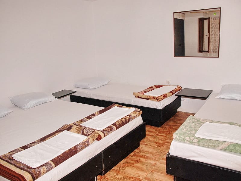 Chambre triple dans une maison à Igalo, Monténégro : trois lits avec linge de maison, miroir mural et sol carrelé.