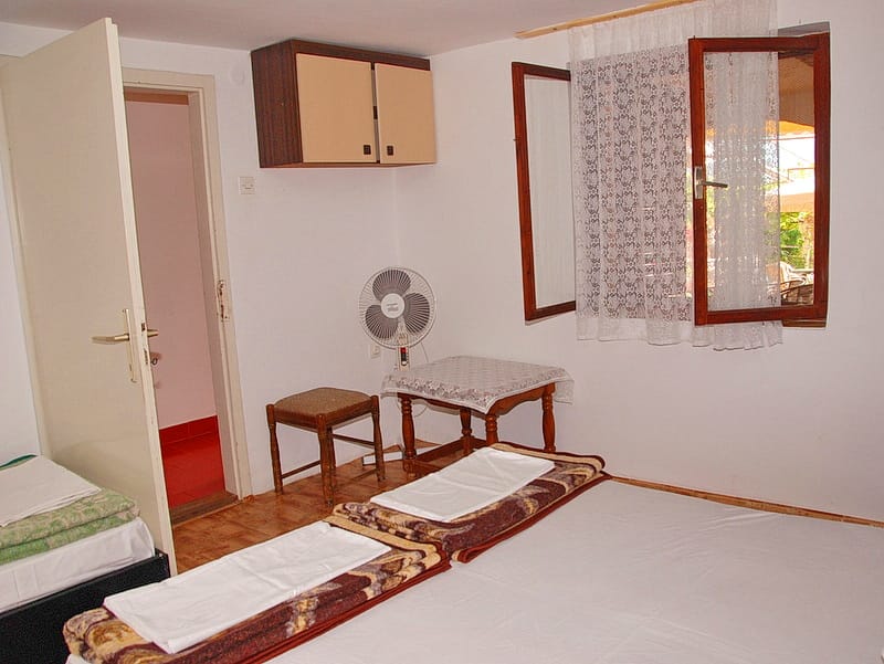 Chambre dans une maison à Igalo, Monténégro : lit double, bureau, chaise, ventilateur et accès à une salle de bain privée.