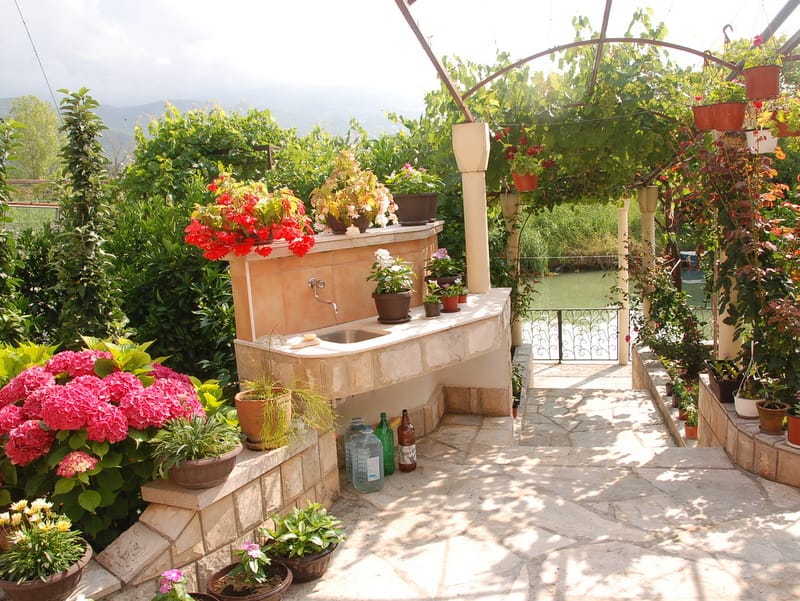 Cuisine d'été dans le jardin d'une maison à Igalo, Monténégro : évier en pierre, hortensias en fleurs et vue sur la rivière depuis la terrasse.