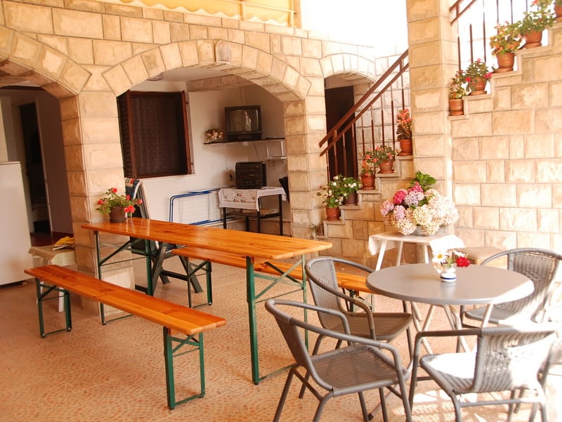 Terrasse couverte avec arches en pierre et mobilier dans une maison à Igalo, Monténégro : coin repas, fleurs et escalier.