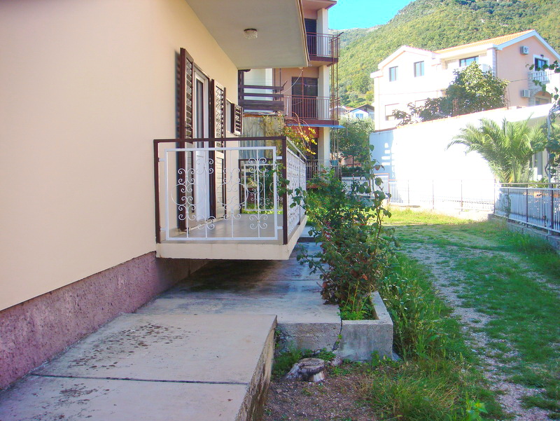 View of a house with a terrace and surrounding grounds in Baošići, Montenegro: white wrought-iron railings and a green garden.
