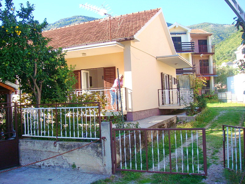 A single-story house with a tiled roof and terrace in Baošići, Montenegro, surrounded by a garden with a lemon tree.