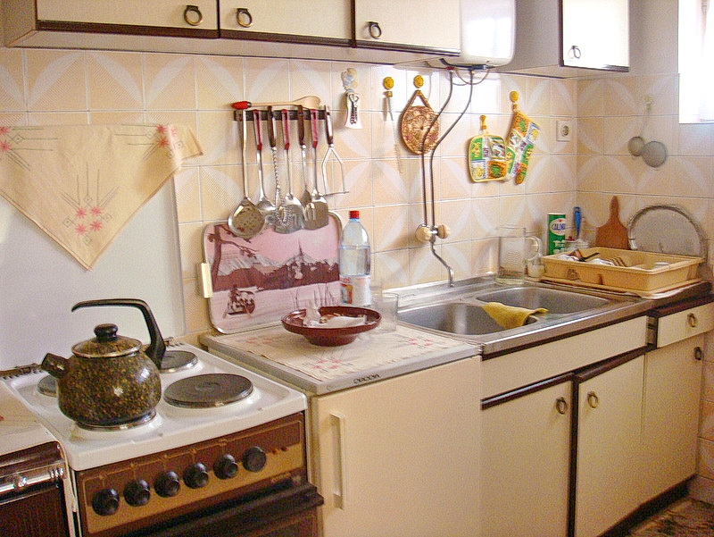 Kitchen in a house in Baošići, Montenegro: light-colored cabinets, electric stove, sink, and kitchen utensils on the wall.