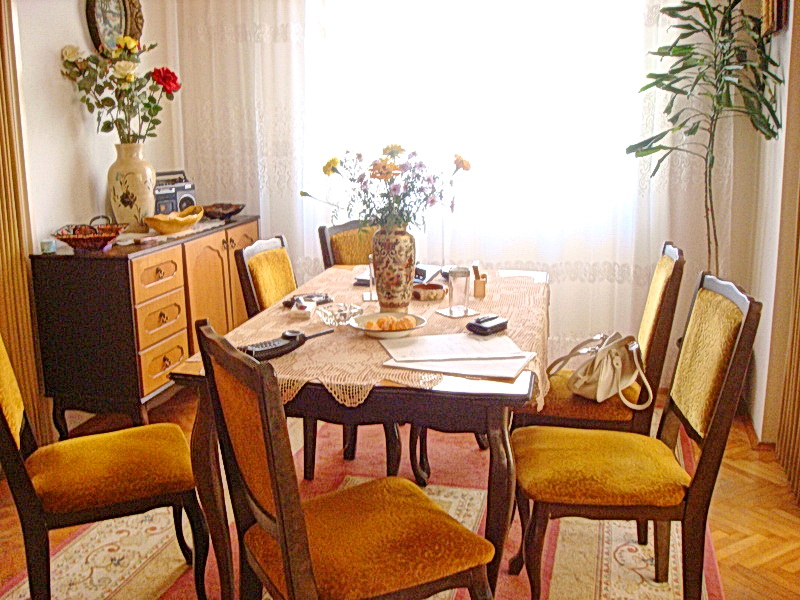 Cozy living room with dining area in a house, Baošići, Montenegro: wooden table, chairs with yellow upholstery, and parquet flooring.