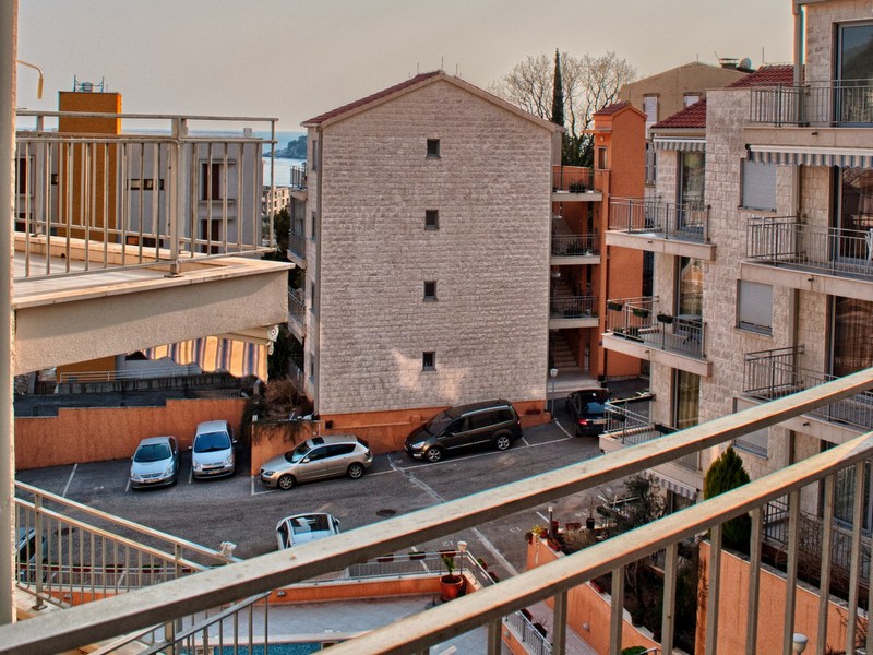 Blick vom Balkon einer Wohnung in Petrovac, Montenegro: moderne Wohnhäuser, Parkplatz und Meereslandschaft am Horizont.