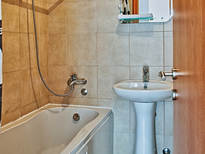 Badezimmer in einer Wohnung in Petrovac, Montenegro: weiße Sanitärkeramik, Badewanne und beige Fliesen in der Innenausstattung.