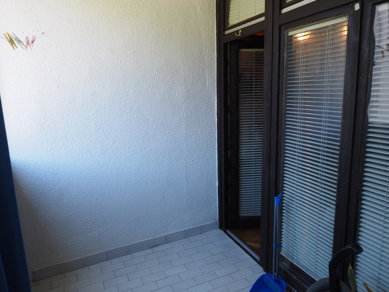 Otvoren balkon sa belom završnom obradom i ulazom u stan u gradu Bar, Crna Gora, sa tamnim okvirima vrata i žaluzinama.