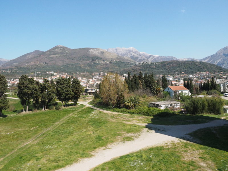 Panoramski pogled na planine i grad Bar u Crnoj Gori sa zelenom površinom i čempresima pored stambenog kompleksa.