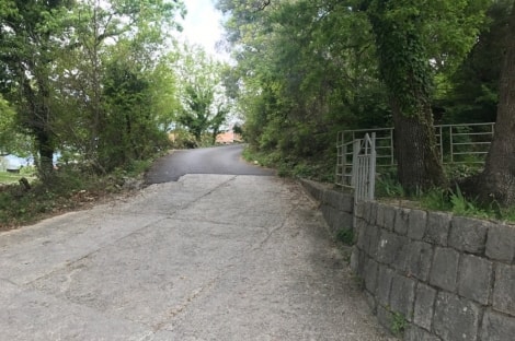 Paved access road to a land plot in Kavac, Montenegro, with a stone retaining wall and trees.