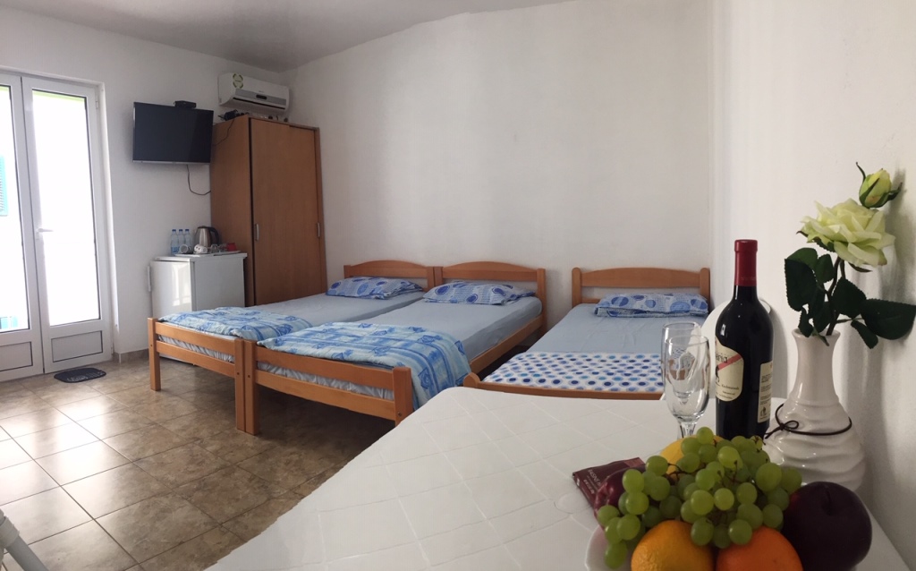 Spavaća soba u mini-hotelu Meline, Crna Gora: tri drvena kreveta, ormar, TV, klima-uređaj i izlaz na balkon.
