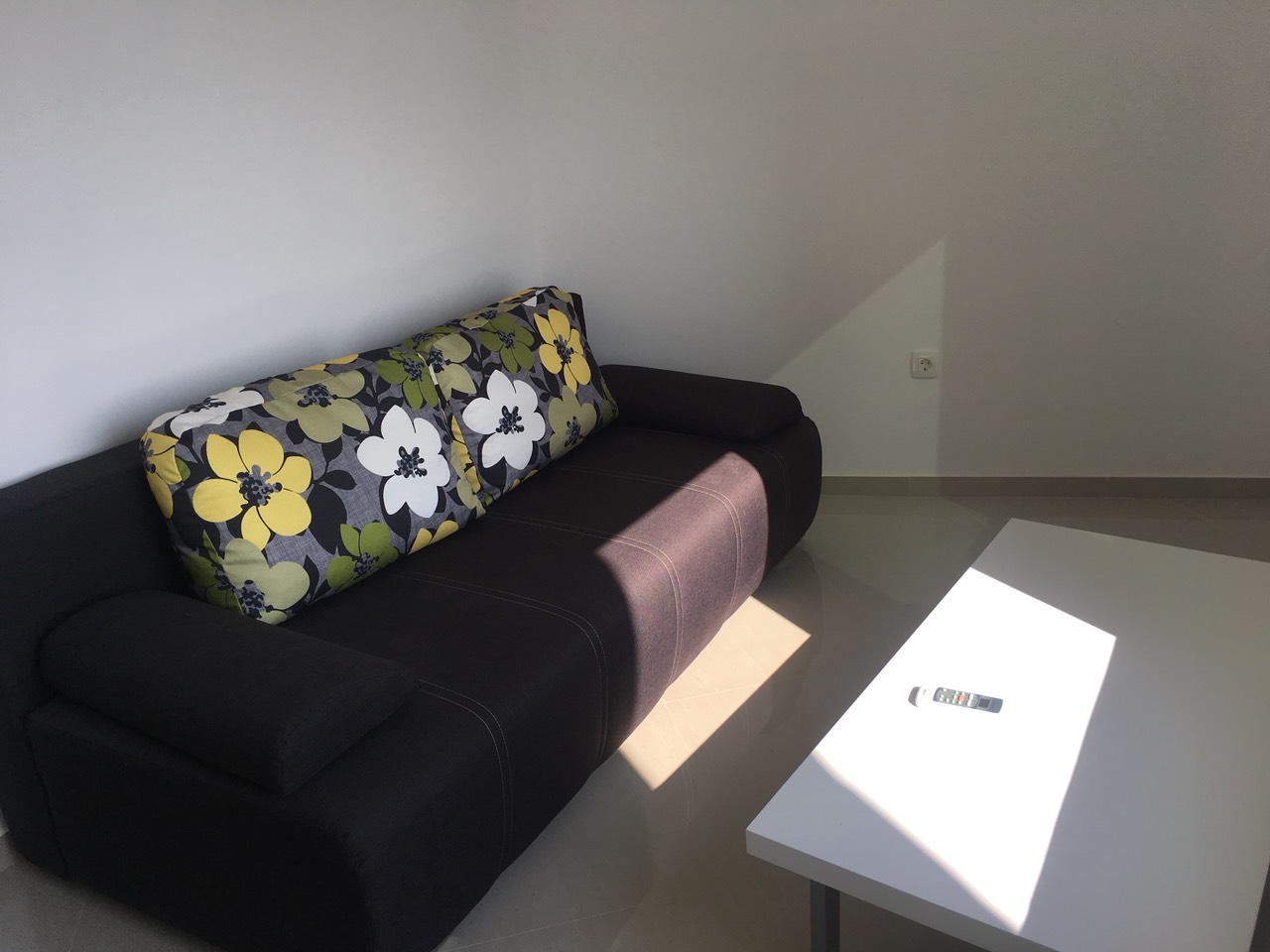 Wohnzimmer mit dunklem Sofa und Blumenmuster im Haus an der Bar Riviera, Montenegro. Helles Interieur, weißer Tisch.