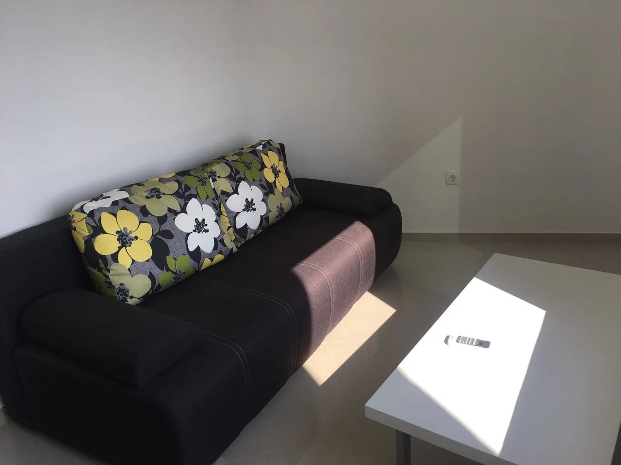 Black sofa with floral cushion and white coffee table in a room with plain white walls.