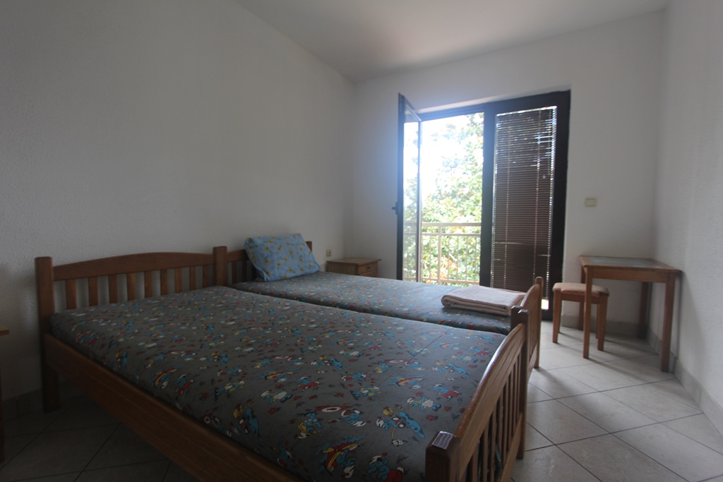 Schlafzimmer im Mini-Hotel Baošići, Montenegro: zwei Holzbetten, Tisch, Fliesenboden und Zugang zum Balkon mit Aussicht.