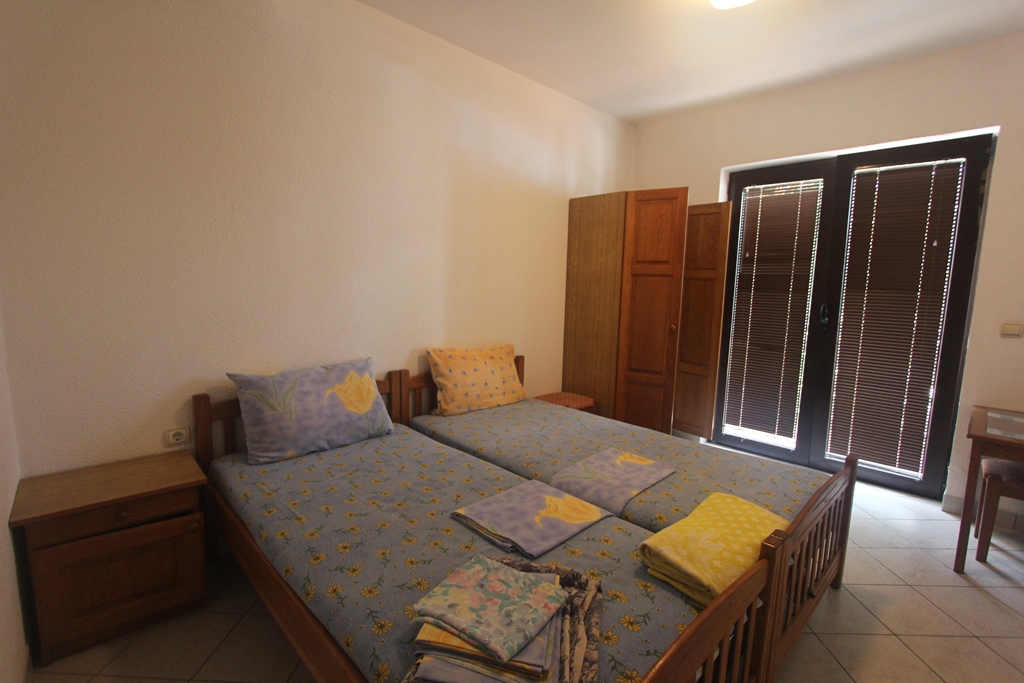 Schlafzimmer mit zwei Betten und Holzmöbeln in einem Mini-Hotel, Baošići, Montenegro. Heller Raum mit Zugang zum Balkon.