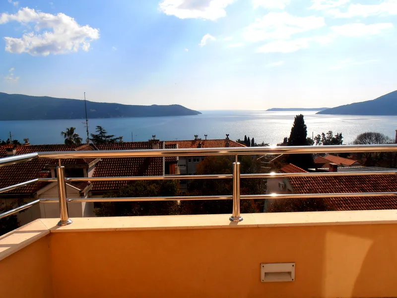 Pogled sa balkona stana u Herceg Novom, Crna Gora: panorama mora, planina i krovova kuća sa crepom.