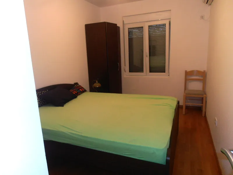 Spavaća soba u stanu u Herceg Novom, Crna Gora: bračni krevet, tamni ormar, drveni pod i prozor sa žaluzinama.