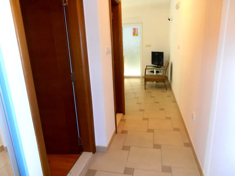 Svetao hodnik u stanu u Herceg Novom, Crna Gora: pločice na podu, drvena vrata i izlaz na balkon sa žaluzinama.