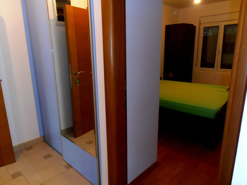 Spavaća soba u stanu u Herceg Novom, Crna Gora: krevet sa zelenim prekrivačem, ormar i unutrašnja vrata od drveta.