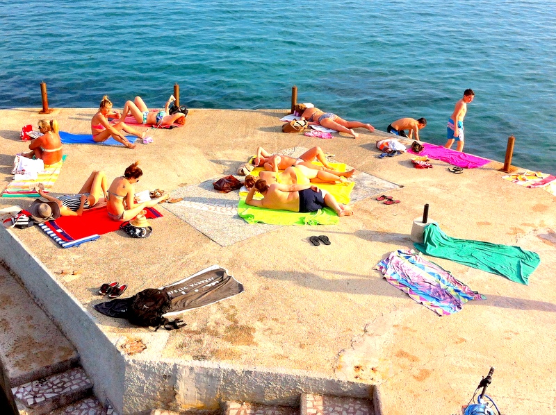 Menschen sonnen sich auf einem Betonsteg am Meer in Herceg Novi, Montenegro, Blick auf den Strand neben Wohnung Nr. 1135.