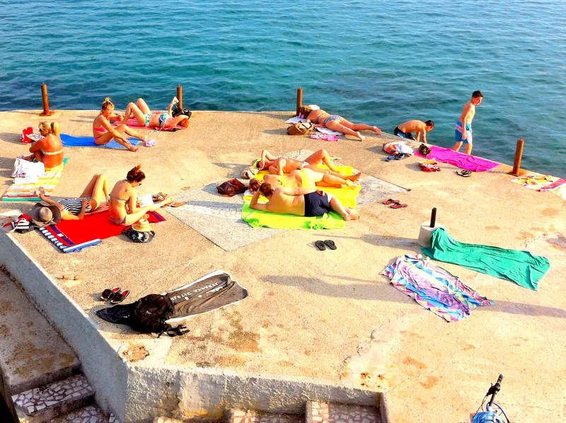 Menschen sonnen sich auf einem Betonsteg am Meer in Herceg Novi, Montenegro, Blick auf den Strand neben Wohnung Nr. 1135.