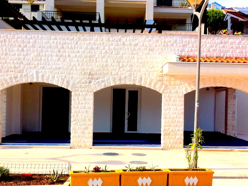 Fassade eines Hauses aus weißem Stein mit Bogenterrassen in Herceg Novi, Montenegro: Blick auf die Wohnanlage von der Straße aus.