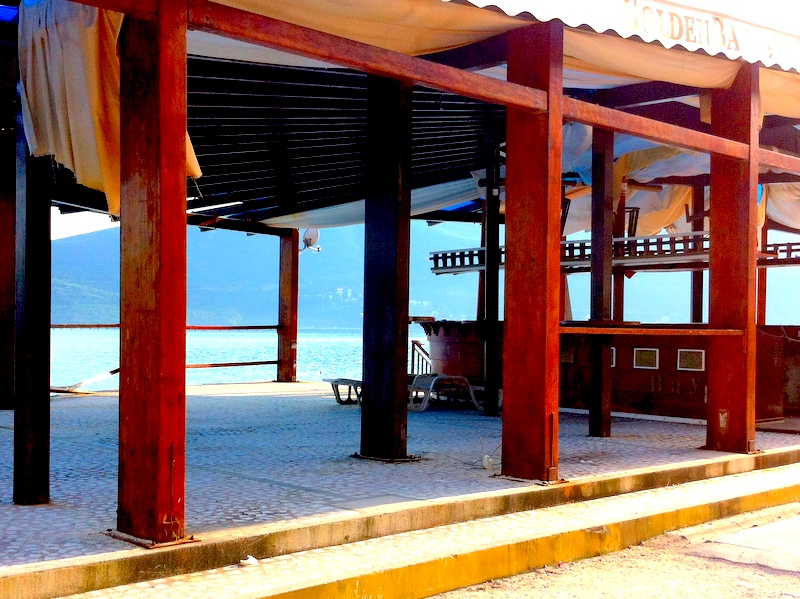 Offene Restaurantterrasse am Meer in Herceg Novi, Montenegro: Holzrahmen, Überdachung und Blick auf die Bucht und die Berge.