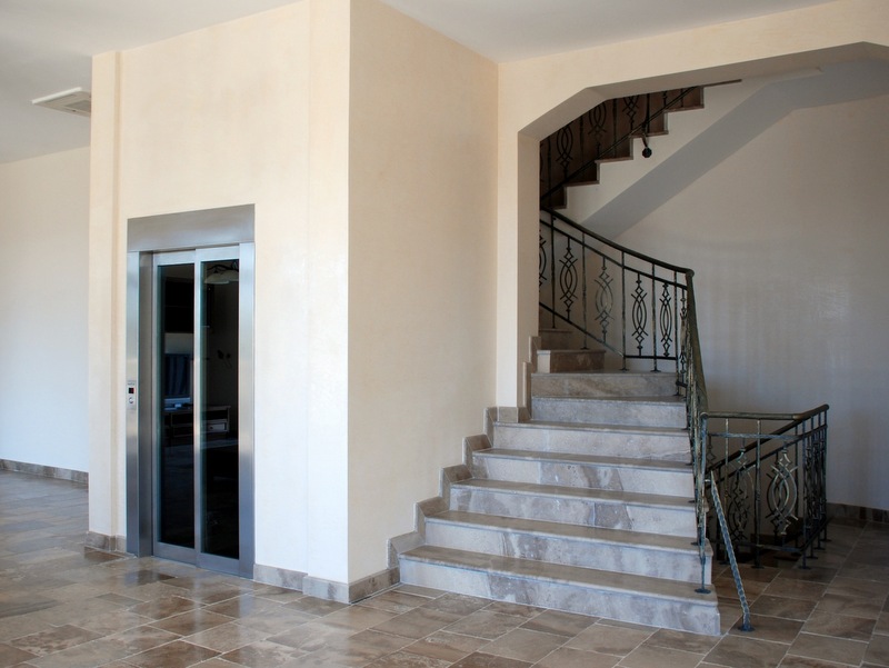 Innenraum einer Villa in Petrovac, Montenegro: moderner Aufzug und Marmortreppe mit schmiedeeisernem Geländer in der Halle.