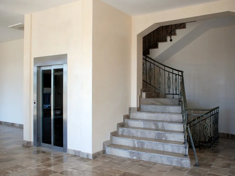 Innenraum einer Villa in Petrovac, Montenegro: moderner Aufzug und Marmortreppe mit schmiedeeisernem Geländer in der Halle.