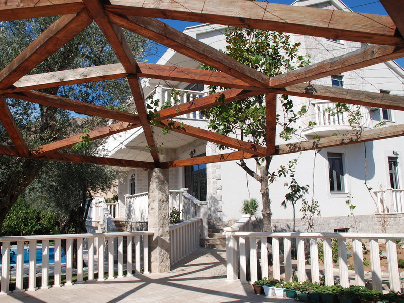 Holzpergola auf der Terrasse einer Villa in Petrovac, Montenegro, mit Blick auf die Hausfassade und den Pool im Garten.