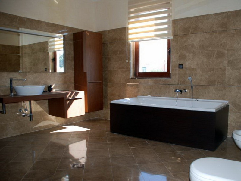 Modernes Badezimmer mit braunen Fliesen, weißer Badewanne und Holzmöbeln in einer Villa in Petrovac, Montenegro.