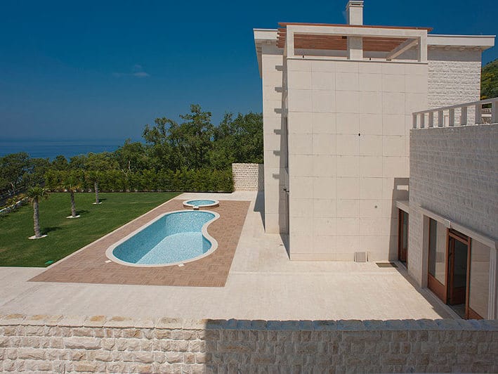 Villa moderne à Reževići, Monténégro : façade en pierre, piscine extérieure, jardin soigné et vue panoramique sur la mer.